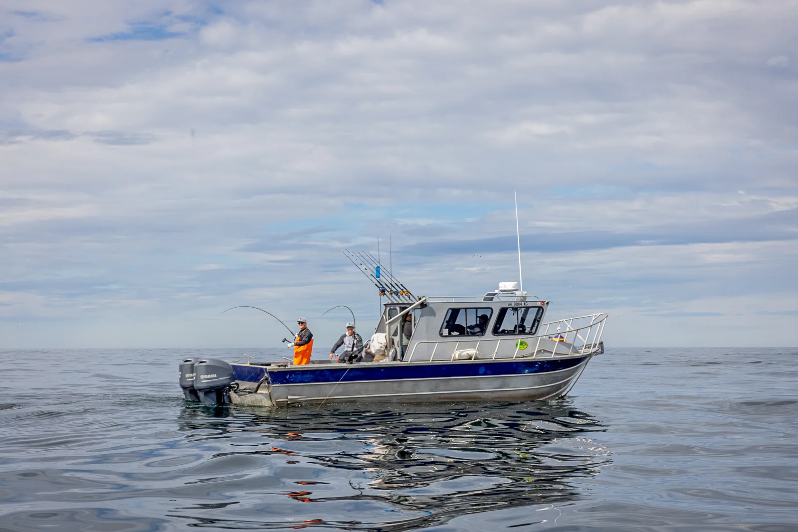 Aluminum charter boat with anglers fishing from the stern on calm open water under a partly cloudy sky.