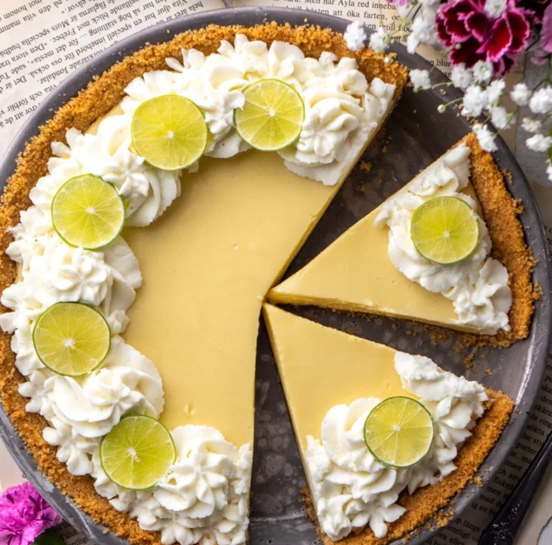 Key lime pie with graham cracker crust, piped whipped cream, and lime wheel garnishes, two slices cut and plated.