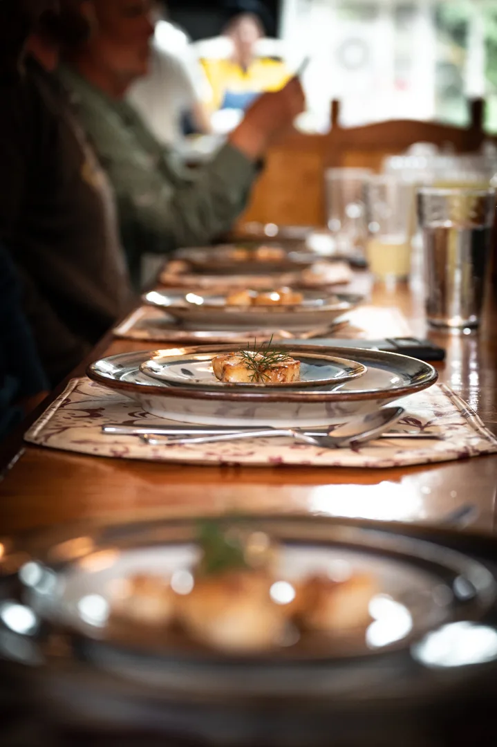 Plated seafood appetizers with dill garnish lined down a long dining table, guests seated in background.