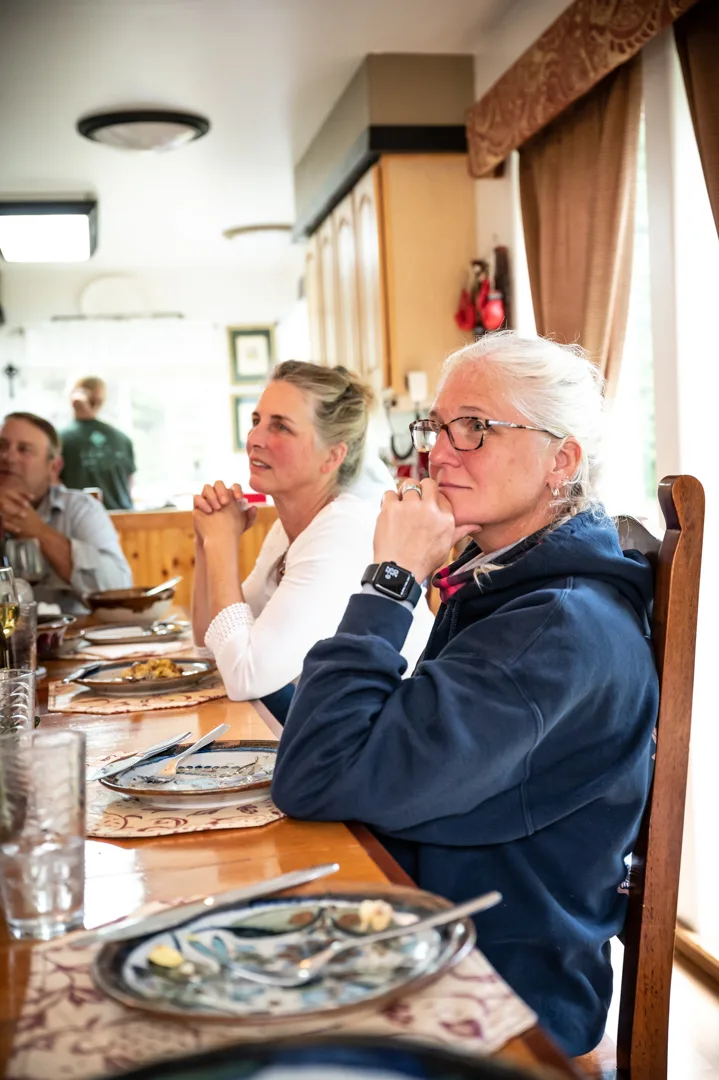 Guests seated at a long dining table inside the lodge, plates cleared, listening attentively.