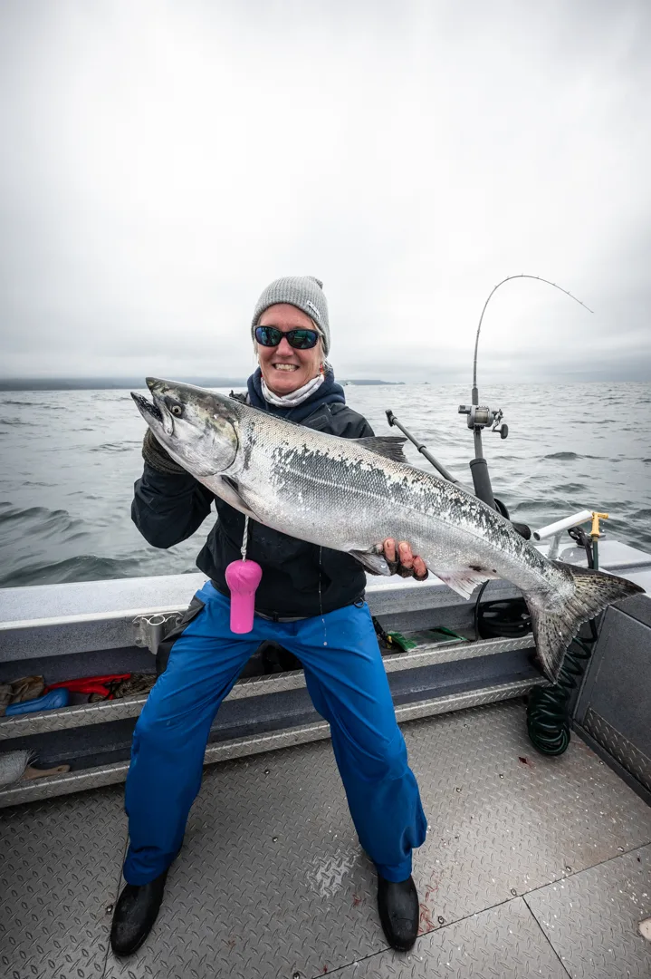 Angler holds a large king salmon on the deck of an aluminum fishing boat, overcast Icy Strait water in the background.