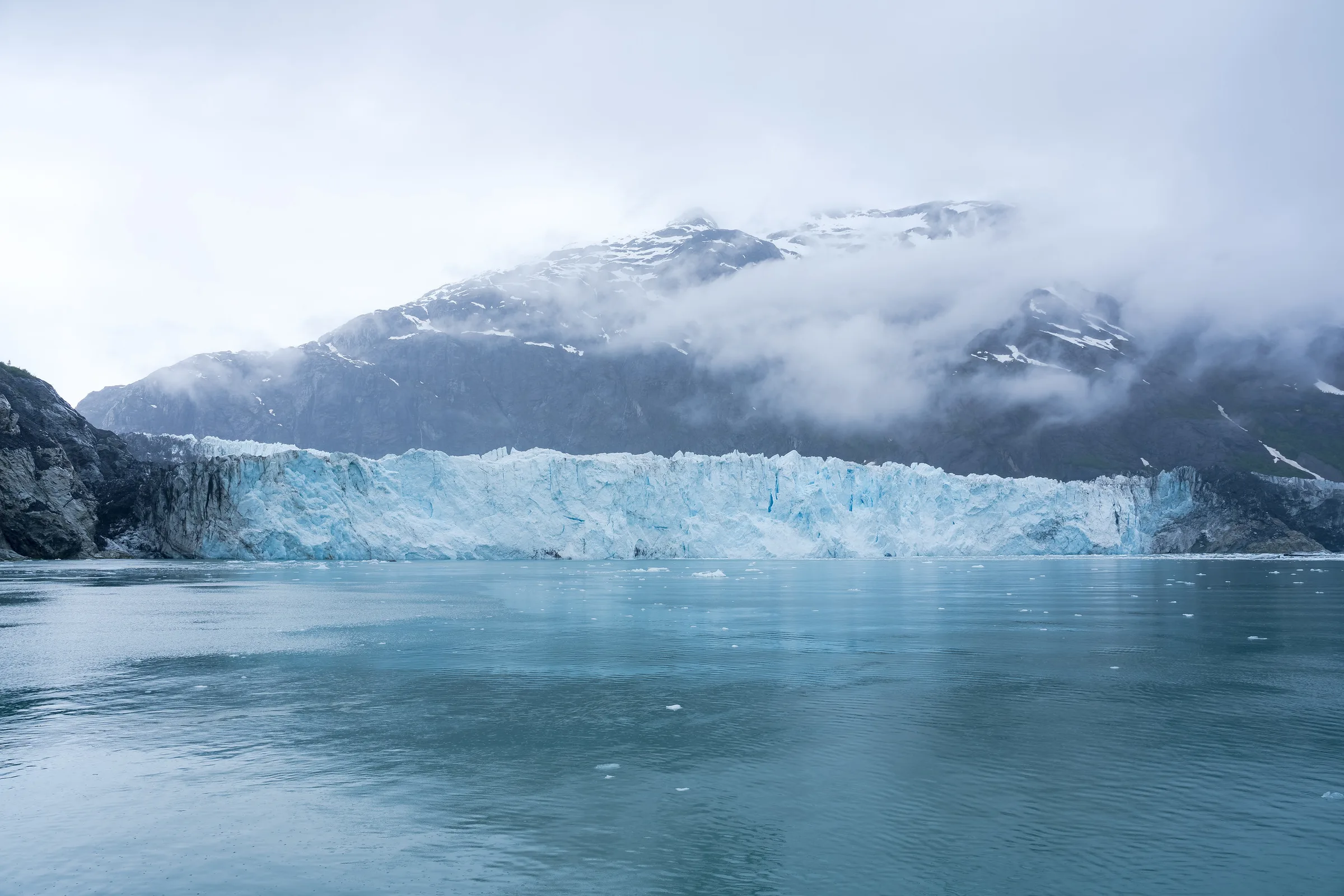 Tidewater glacier face meeting calm water in Glacier Bay, cloud-wrapped mountains rising behind