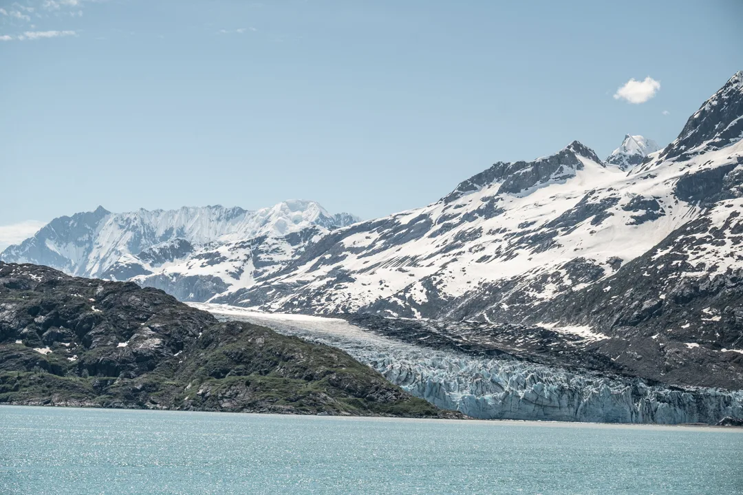 Tidewater glacier descending to glacial blue water, snow-covered peaks rising behind, Glacier Bay National Park.