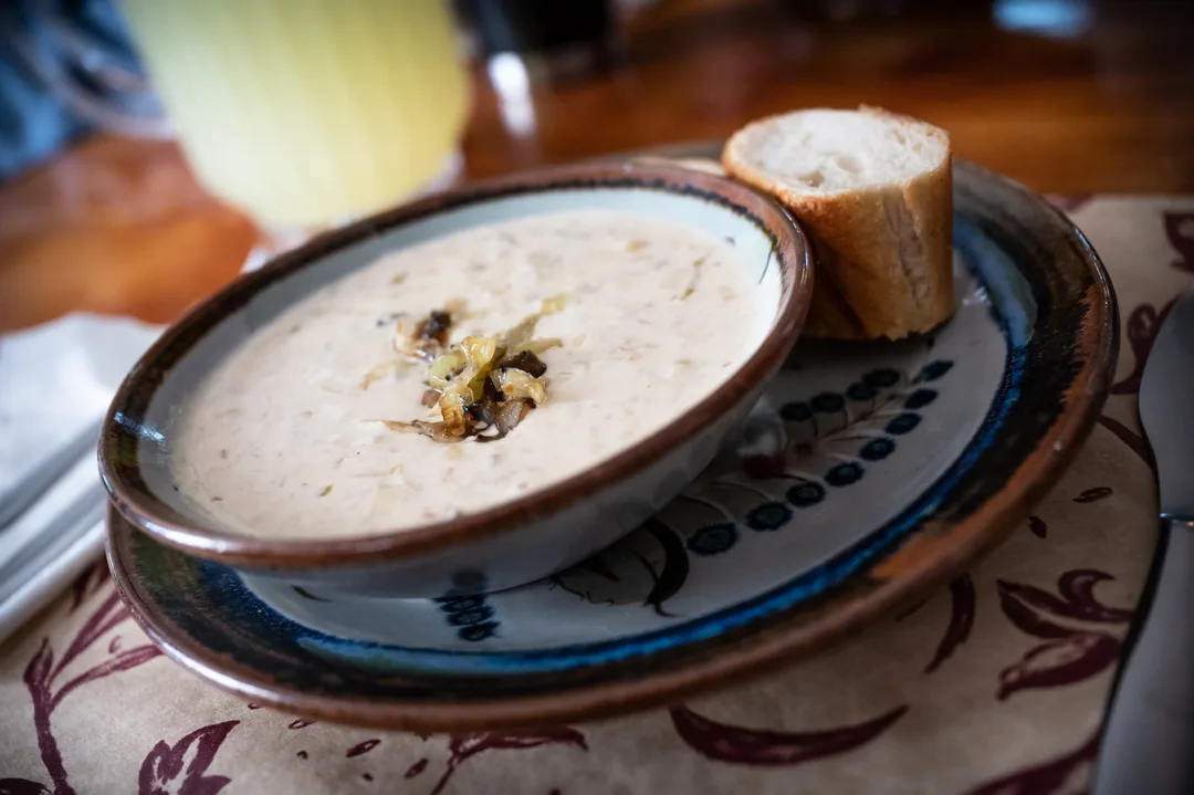 Cream-based chowder in a handmade ceramic bowl with crusty bread on a patterned stoneware plate