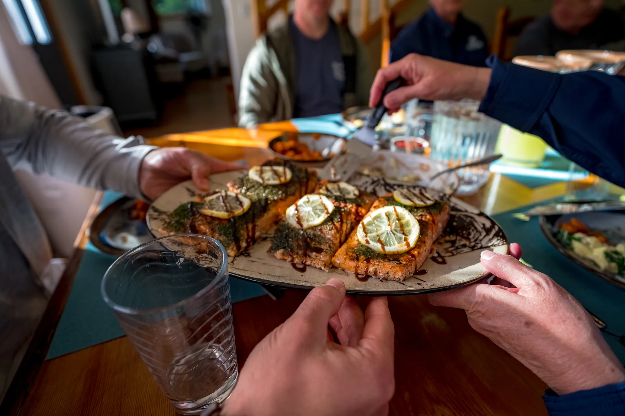 Platter of herb-crusted salmon fillets with lemon slices passed around the dining table.