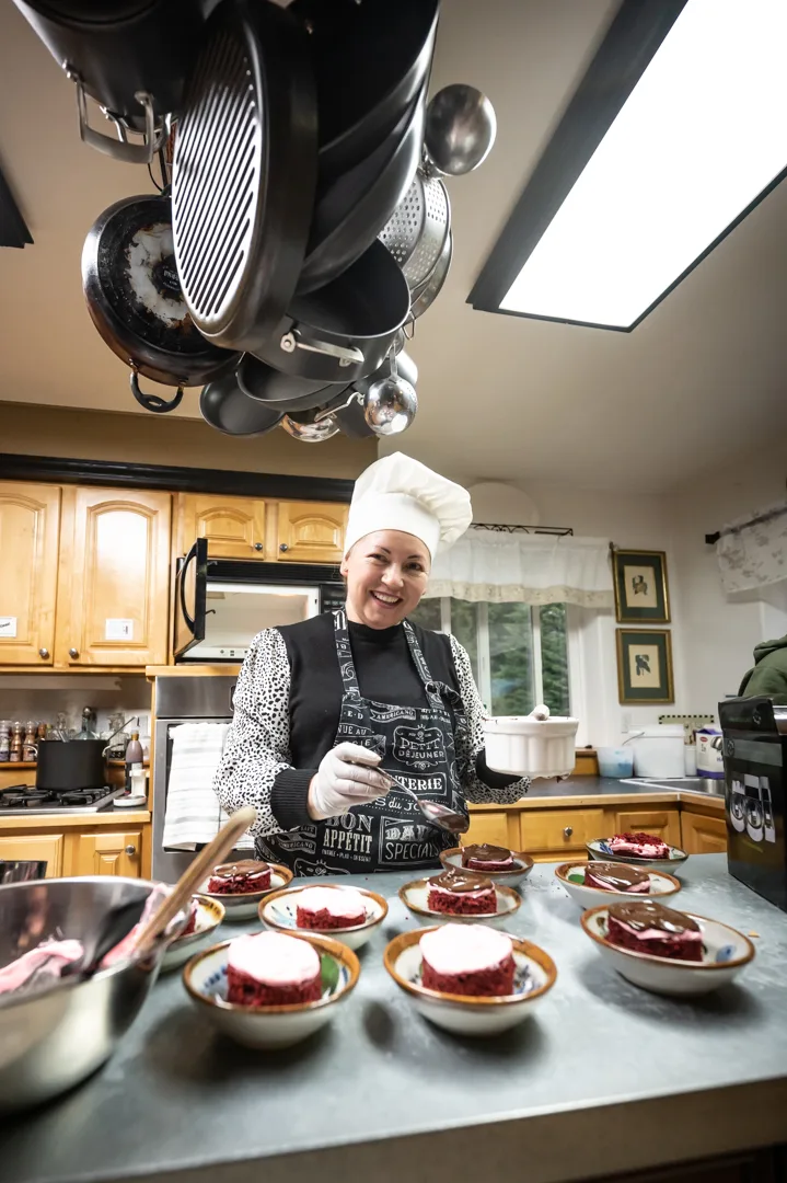 Chef in white toque plating individual red velvet cake desserts with chocolate sauce in lodge kitchen