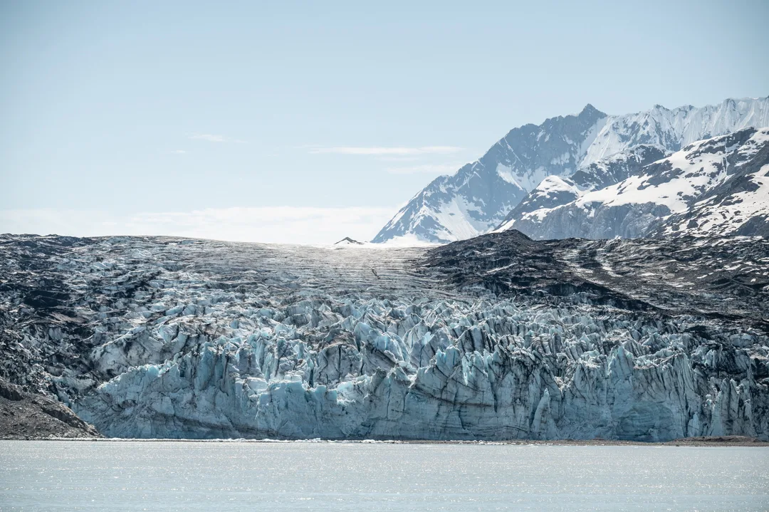 Tidewater glacier face meets calm water, snow-capped peaks rising behind, Glacier Bay National Park