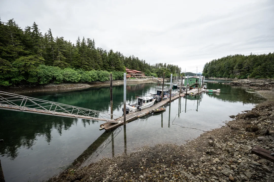Lodge building and private dock with fishing boats moored in a calm forested cove at low tide, Southeast Alaska.